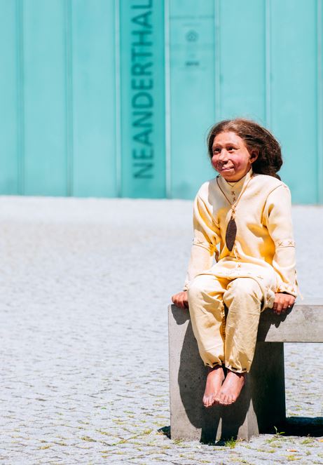 Neanderthaler-Mädchen Kina sitzt vor dem Museum auf einer Steinbank.